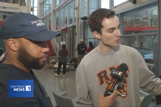 an R I T student appears with a Spectrum News anchor who is holding a mic.