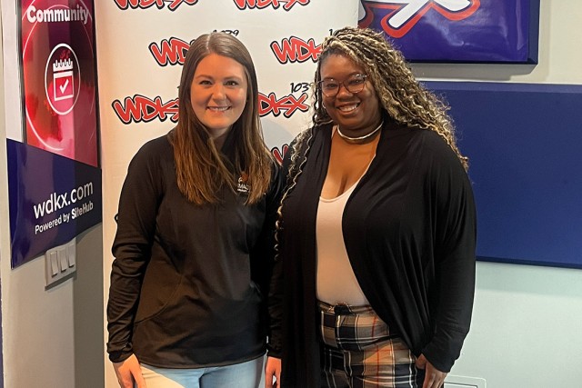 Ann Ielapi and Shaneil Davila are pictured standing in front of a poster that has a WDKX logo printed on it repeatedly.