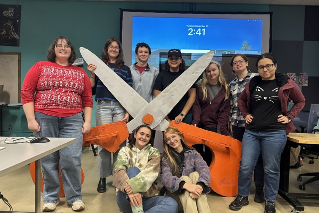 Students pose with a giant pair of orange scissors.
