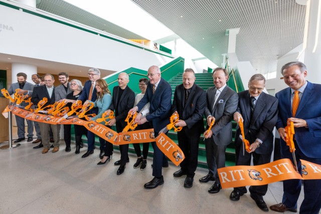 Group of officials cut orange R I T ribbon during building opening ceremony indoors