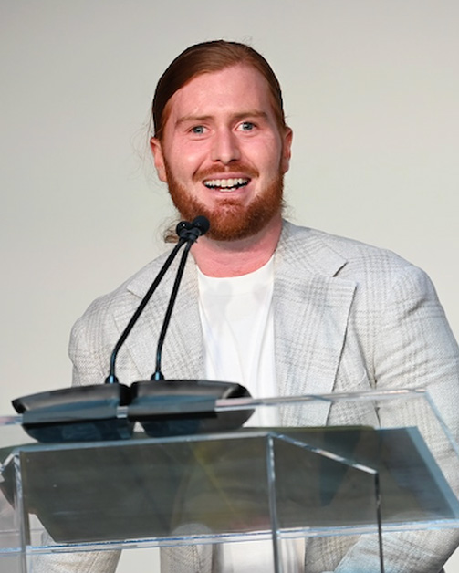 a man standing at a podium, smiling.