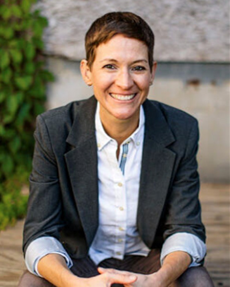 a smiling person wearing a button up white shirt and a gray jacket.