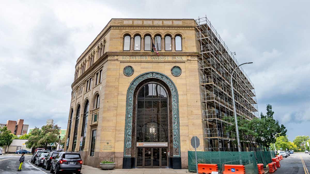 A historic stone building labeled Rochester Savings Bank stands on a city corner with scaffolding along one side.