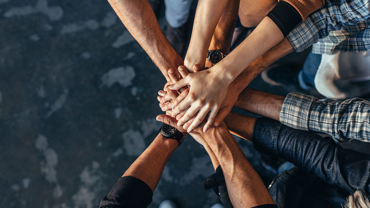 A group of people stack their hands together in a gesture of teamwork and unity.