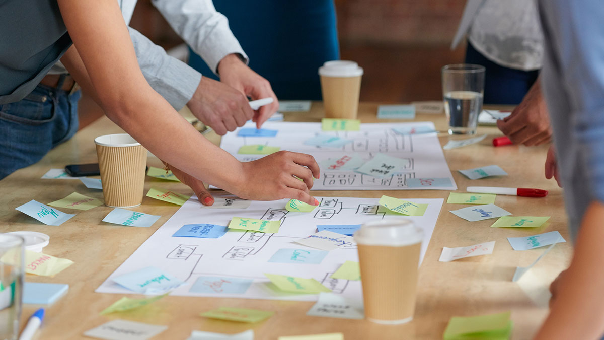 A group of people collaborate around a table covered with notes and diagrams while planning a project.