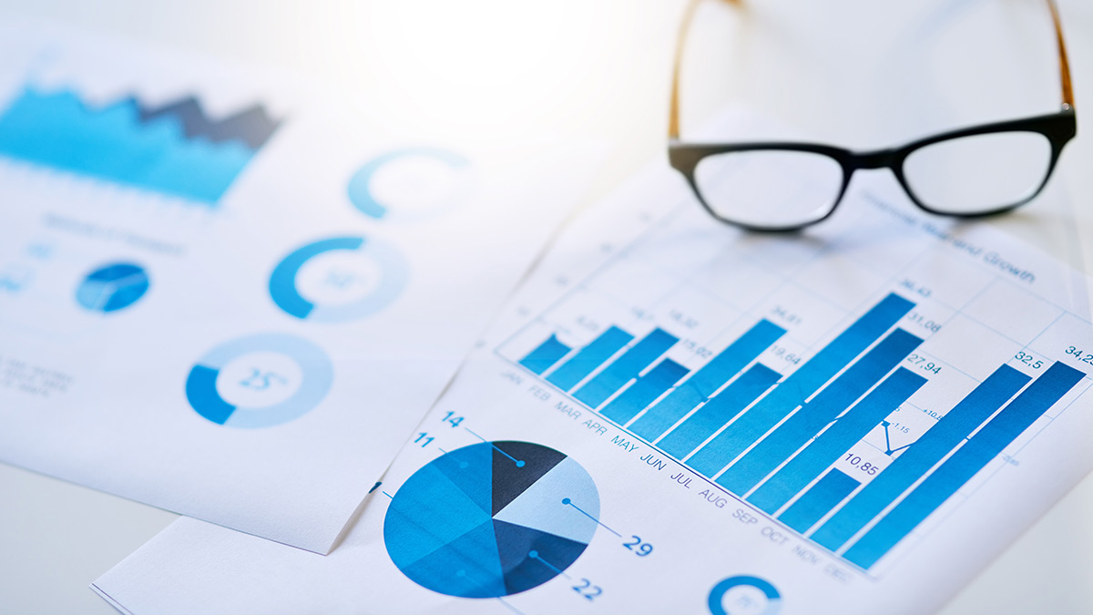 Printed charts and graphs in blue tones lie on a desk beside a pair of glasses.