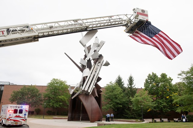 firetruck ladder extended over campus statue with large American flag flying from the bucket.