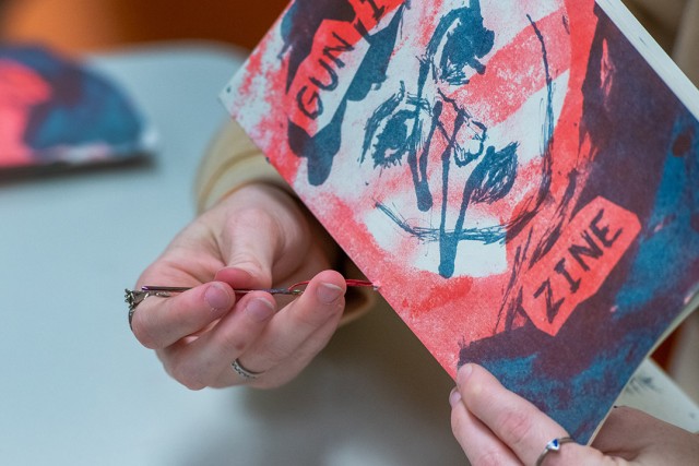 close up of a person's hands holding a paper booklet and threading a needle through the spine.