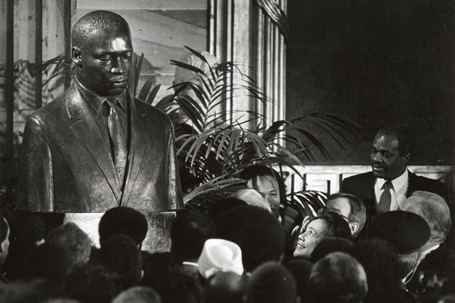 a black and white image of a group of people facing Coretta Scott King as she reacts to an MLK portrait being unveiled