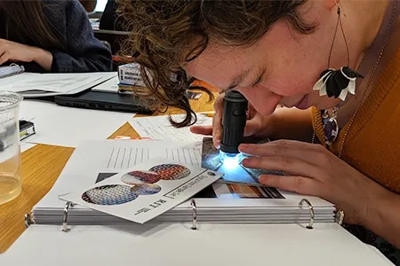 A person sitting at a table looking through a device that has a flashlight at an image.