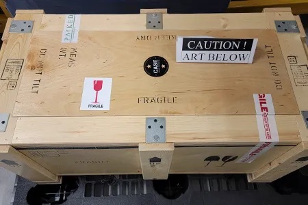 A wooden crate with labels such as "Caution! Art Below", "Fragile", and "Do not tilt".