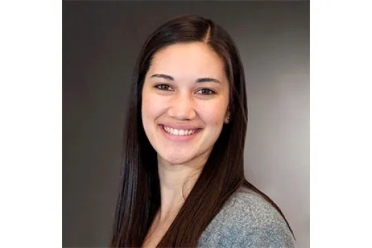 Portrait of Meridith Sharp. Sharp has long dark hair and is in front of a grey background.