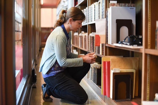 Researcher examining row of books in a library.