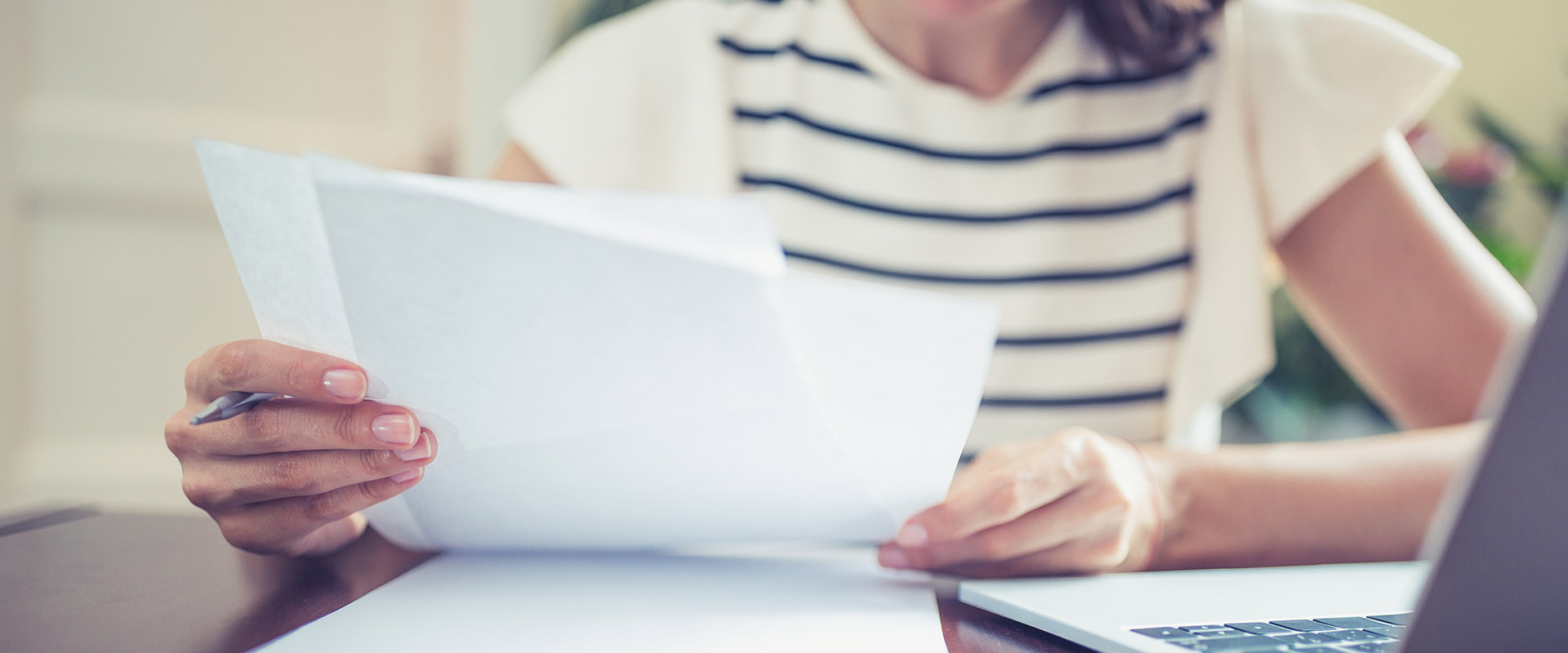 A closeup of a person holding sheets of paper in front of a laptop.