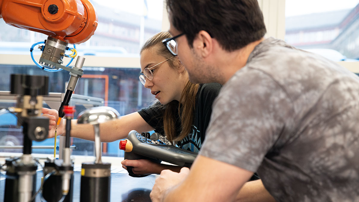 two students work with a robotic arm holding a pencil.