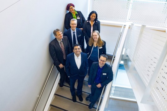seven people stand in a brightly lit white stairwell