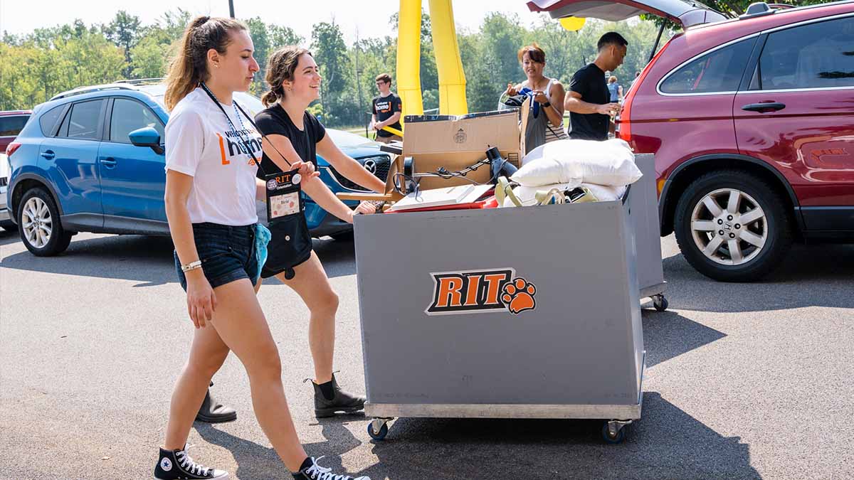two college students walking a rolling cart during move-in day.