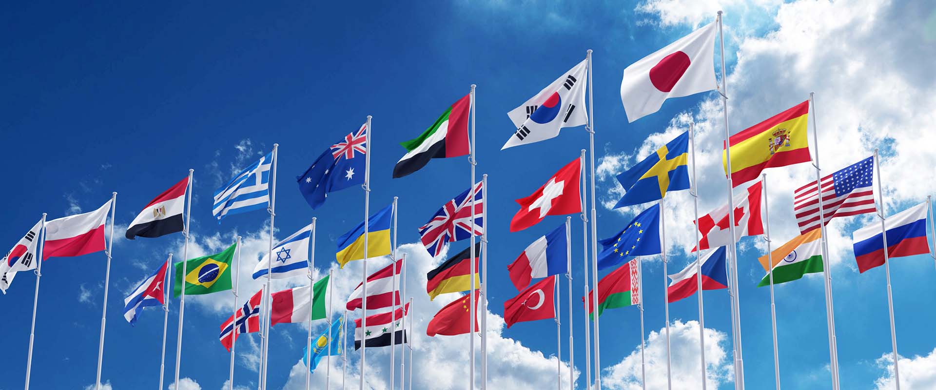 A view looking up at the flags from various nations flying on flag poles.