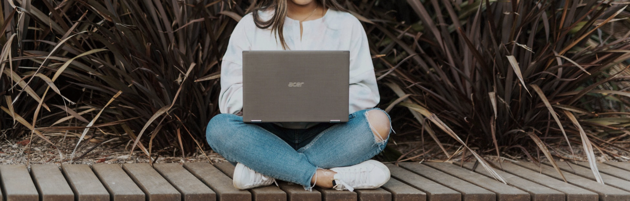 Girl typing on a computer outside by a plant