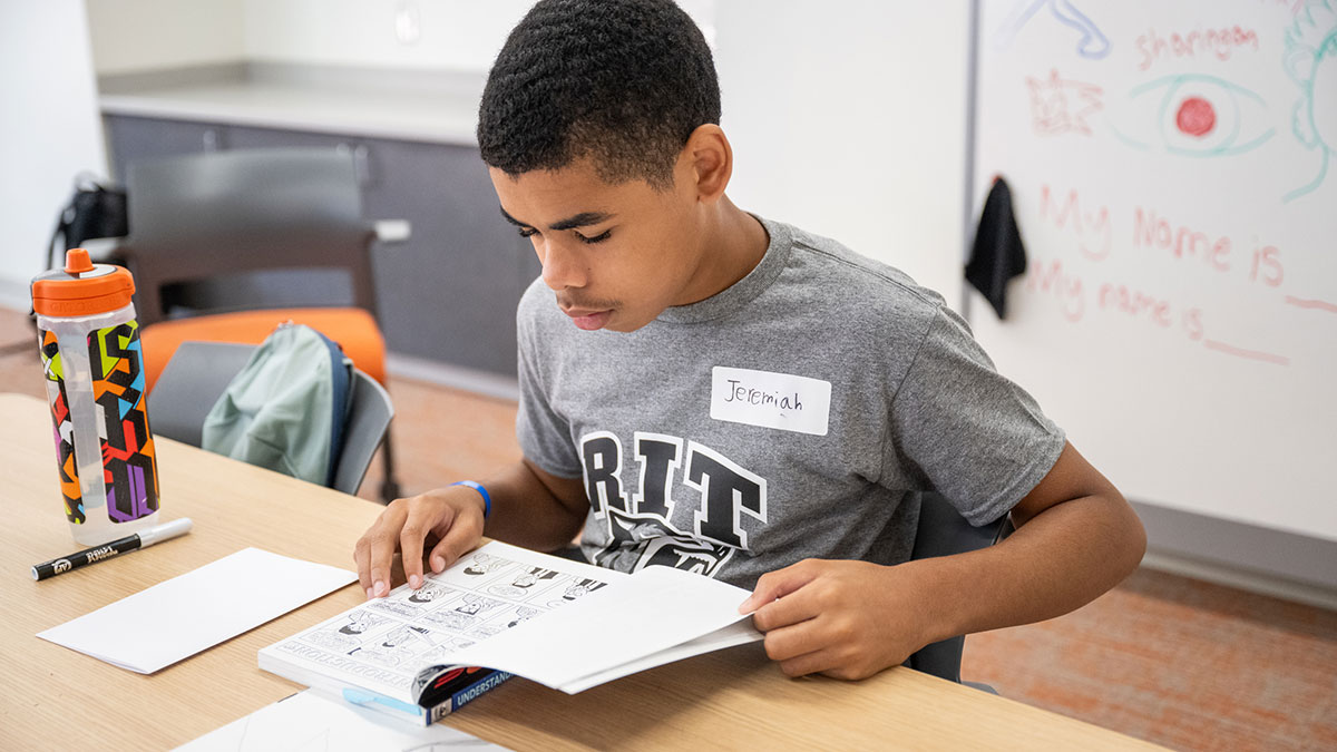an elementary school student reading a comic book at a table.