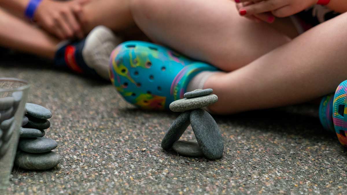 Close-up of a child wearing colorful Crocs stacking smooth stones on the floor.