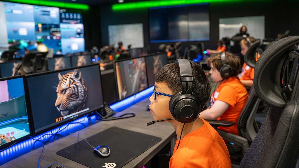 A boy wearing headphones plays a video game at a computer station in an esports lab.