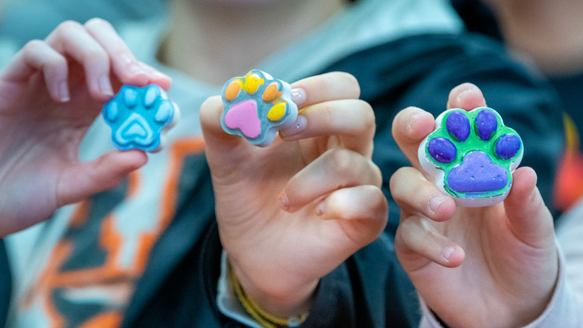 Children hold up colorful paw-shaped tokens decorated in blue, pink, orange, green, and purple.