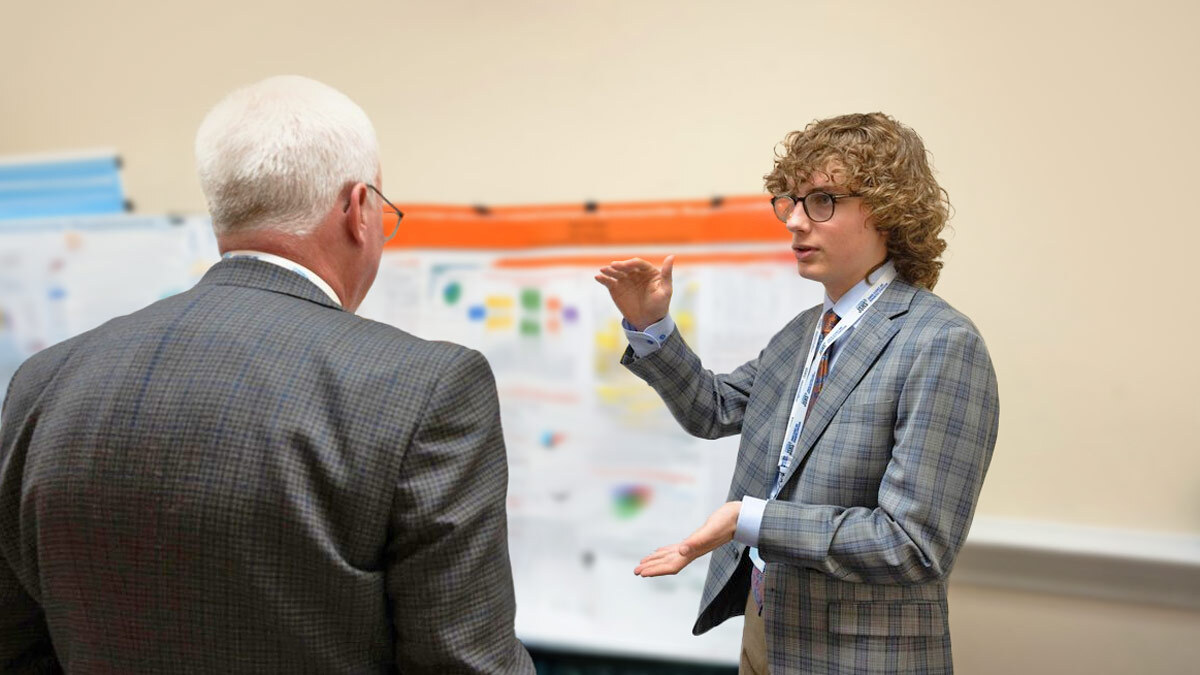 a high school student gives a poster presentation to an older man.