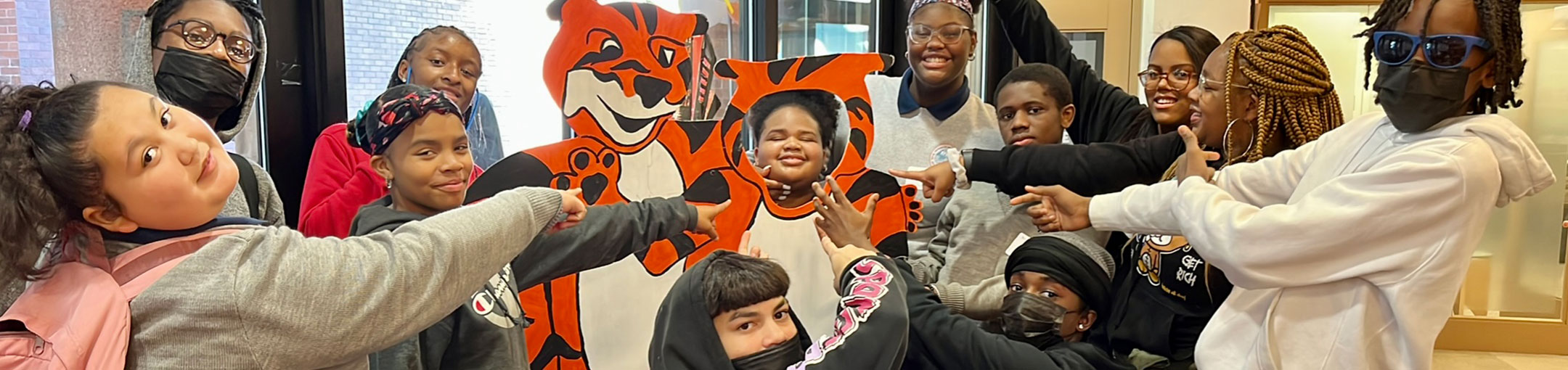 a group of people all pointing to the middle where someone is behind a tiger cutout