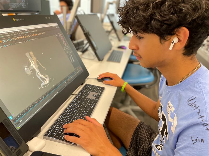 Boy sitting at a computer working on a 3D project in a computer lab. 