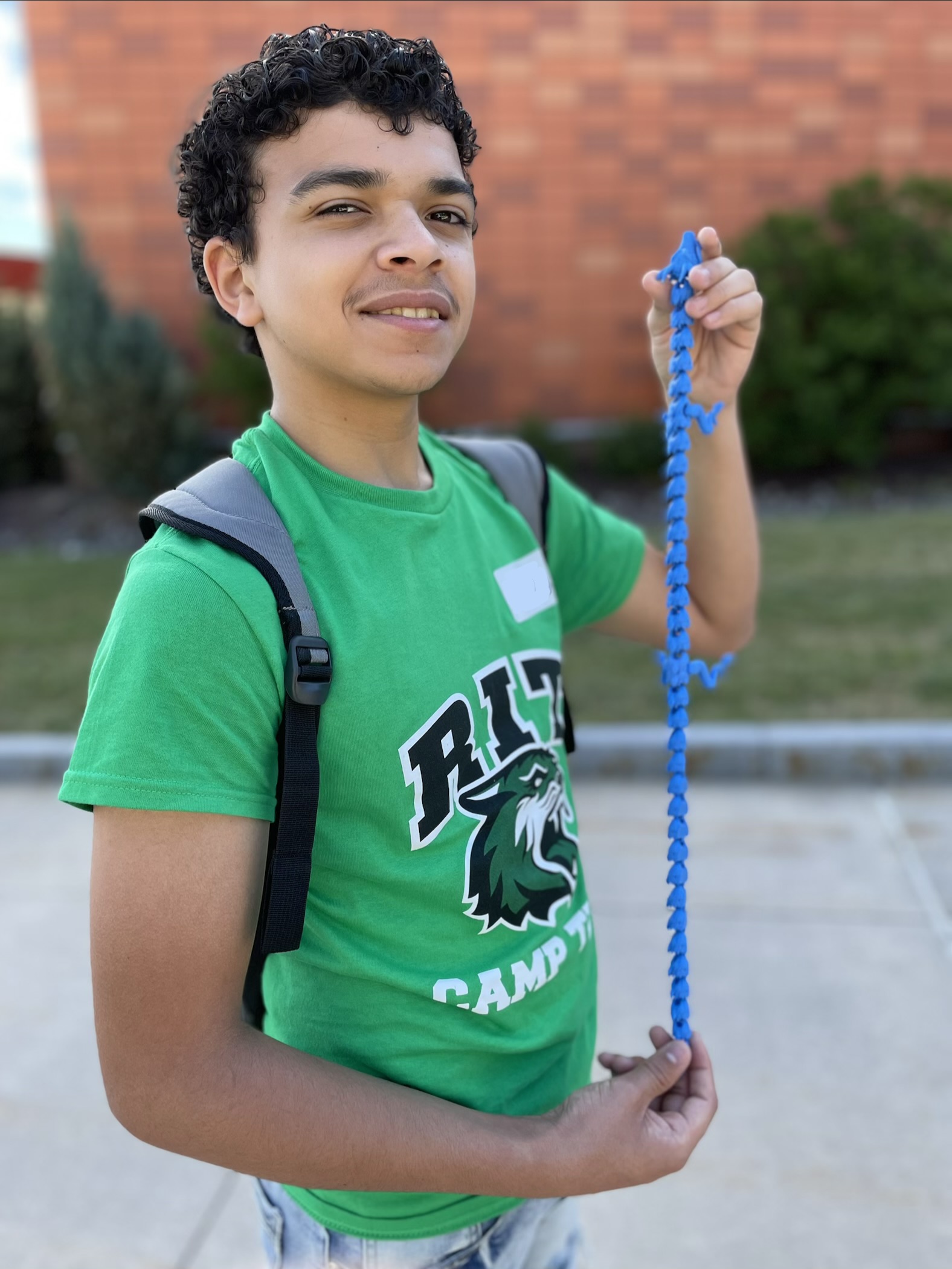 Boy in a green RIT Camp Tiger T-shirt holding a 3D printed blue prehistoric lizard..