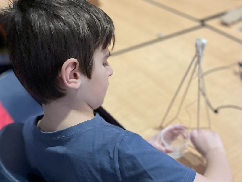 A boy building a pulley system on a table in a classroom. 