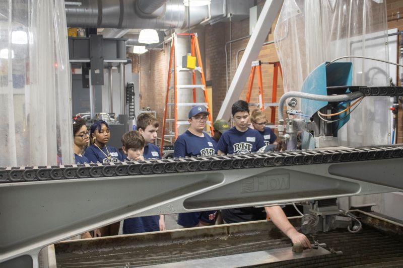 A group of youth learn about machines in RIT's Brickman Lab with a staff member.