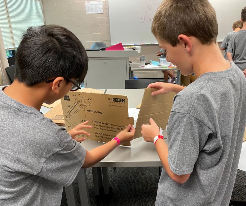 Two boys working together using cardboard on a project in a classroom.