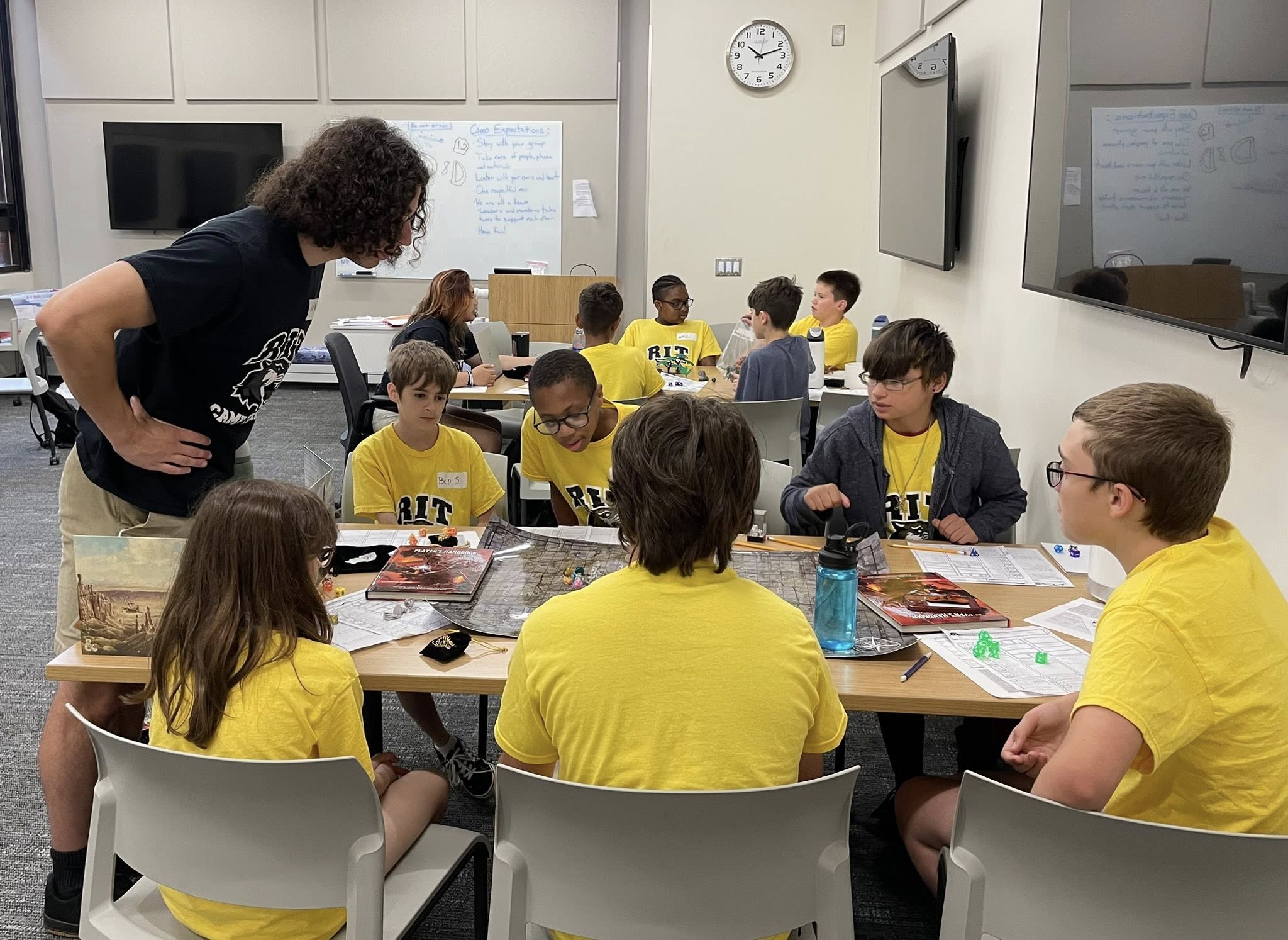 Staff working with campers on Dungeons and Dragons campaigns, seated at two tables.