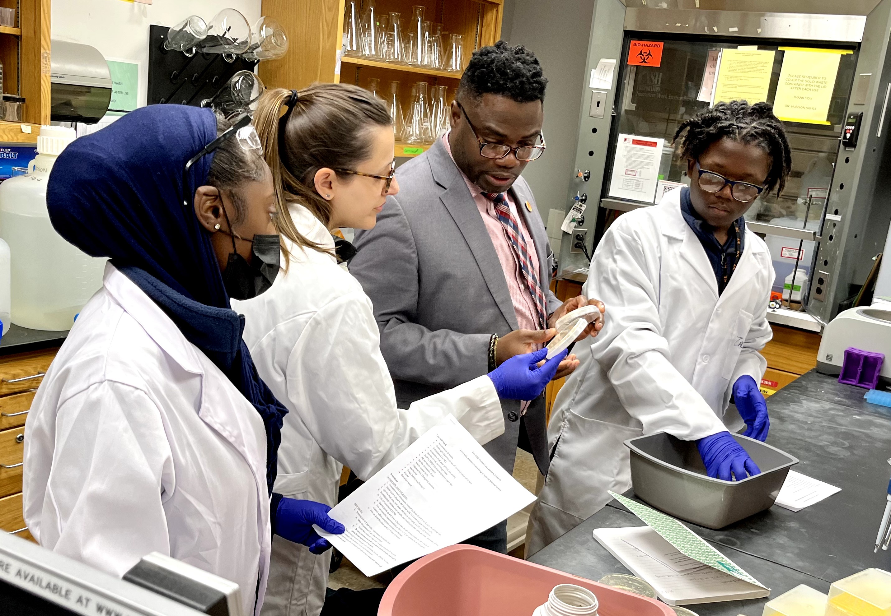 Several students in lab coats working in a lab with faculty on research project.