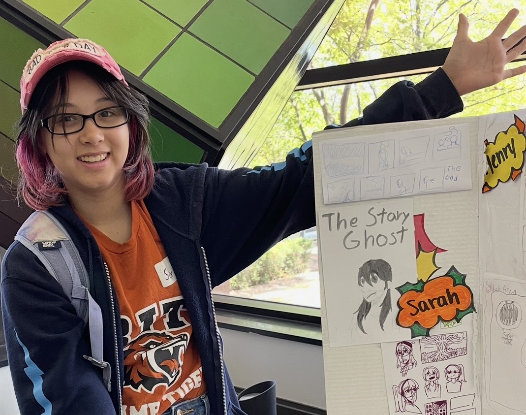 Youth in baseball hat and RIT camp t-shirt displaying their Manga art examples.