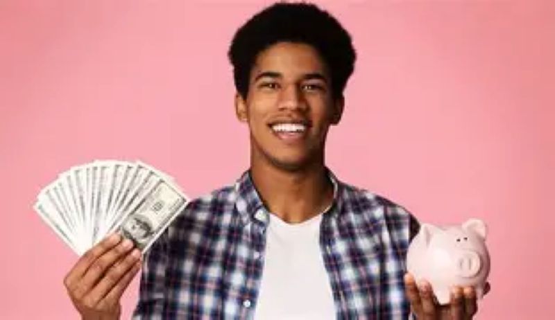 Teenage boy in plaid shirt holding dollar bills and piggy bank.