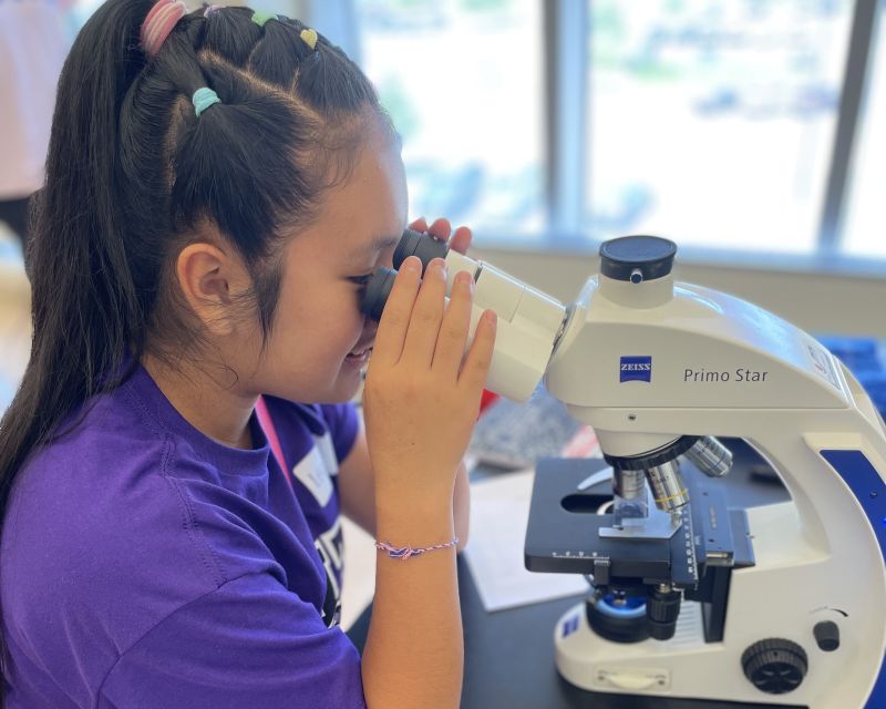 Teen looking in a microscope in a lab. 