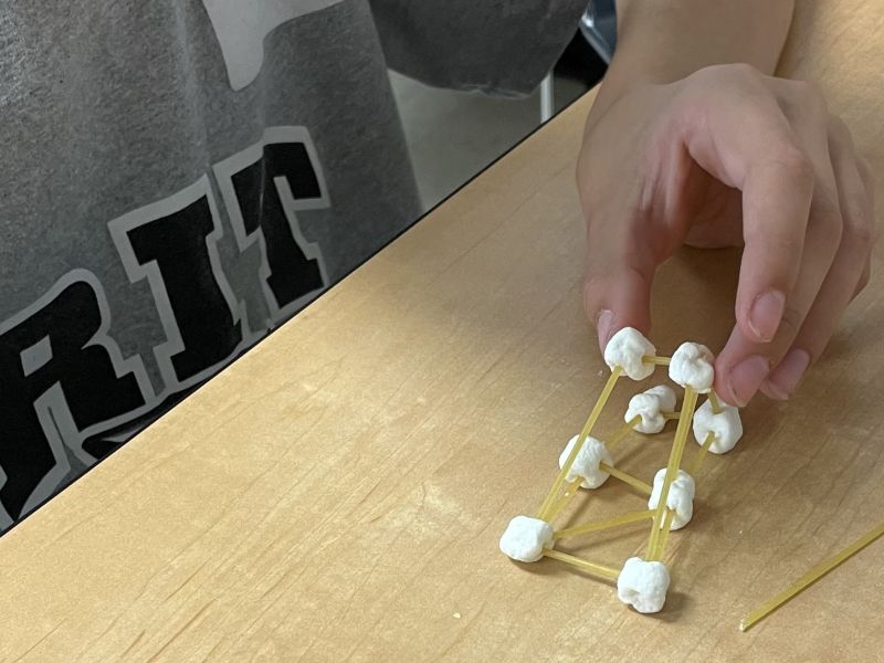 Close up of a youth building at tower with spaghetti and marshmallows.
