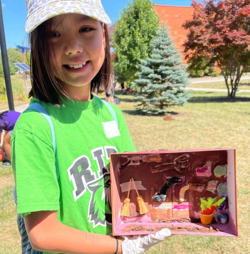 Camper displaying her zoo design diorama  project outdoors. 