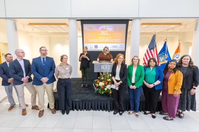 a group of people stand on a small stage with a podium displaying an R I T sign