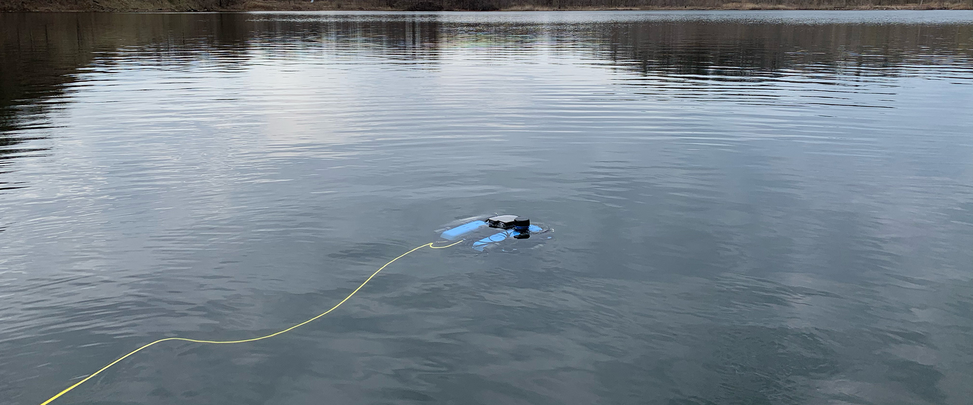 A blue drone floating in a body of water, with trees in the background.