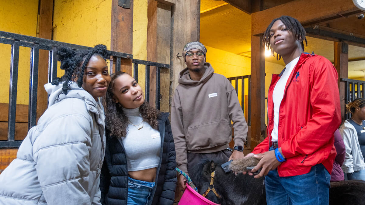 Four students pose for the camera in a horse stable