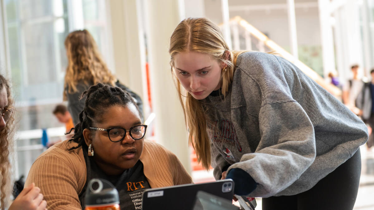 A student and RIT staff look at a laptop during an event for volunteering