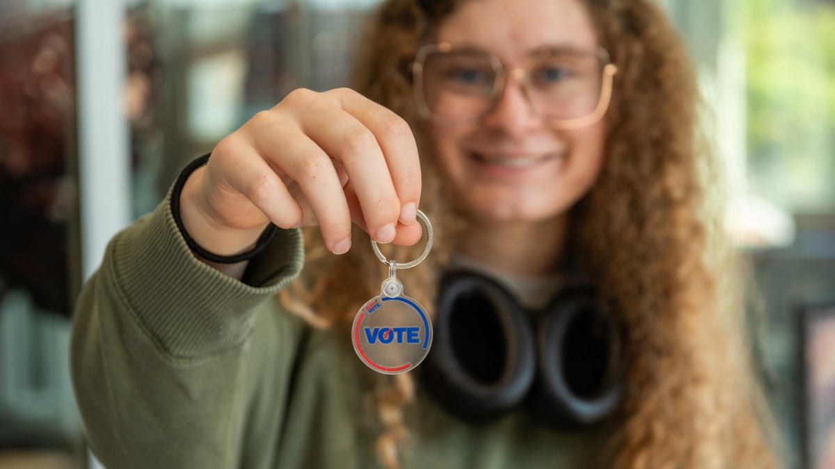 Student smiling and holding up a Roar the Vote keychain to the camera