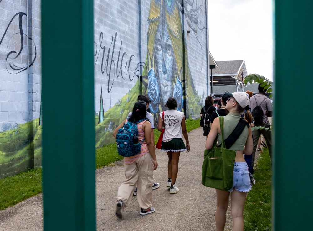 A group of students walking and looking at a mural on a downtown Rochester building during an art tour 