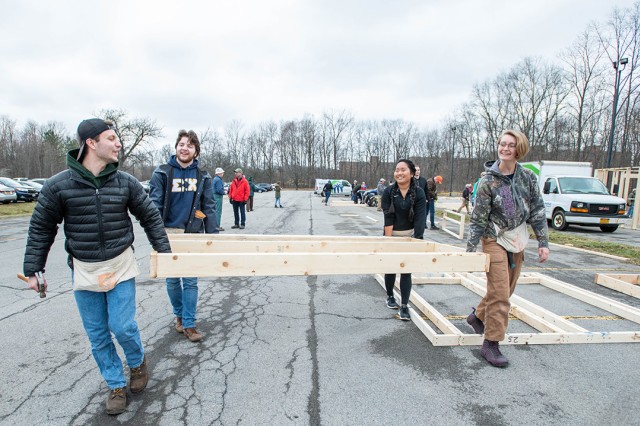 Four students walk through parking lot with wall frame.