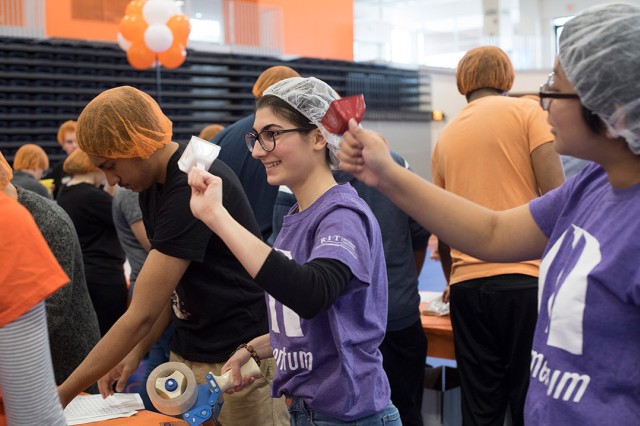 Students wearing hairnets in assembly line ring cowbells.