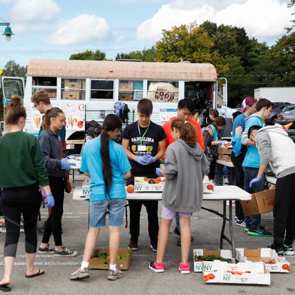 students crowding around tables of produce at a public market.